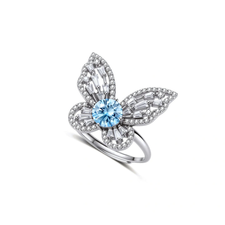 Sterling silver ring with blue moissanite center stone surrounded by clear stones in butterfly wing pattern on white background